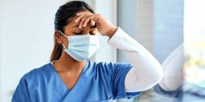 photo of tired nurse, wearing a mask, with hand against forehead